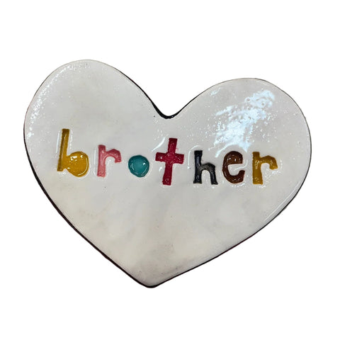 Heart-shaped object with 'brother' in colorful letters held by a hand on a concrete surface.