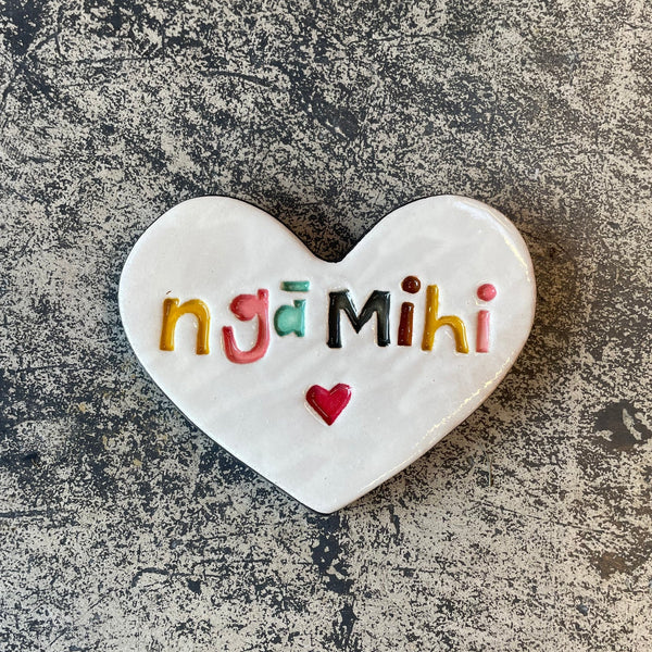 Heart-shaped ceramic tile with 'ngá Mihi' in colorful letters on a textured surface