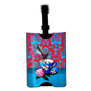 Luggage tag with a colorful design featuring a teacup and flowers on a red and blue patterned background.